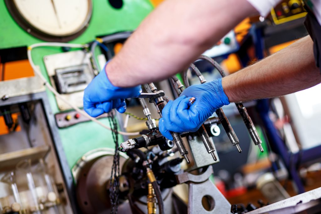 Mechanics servicing a diesel engine injector in a close-up shot.