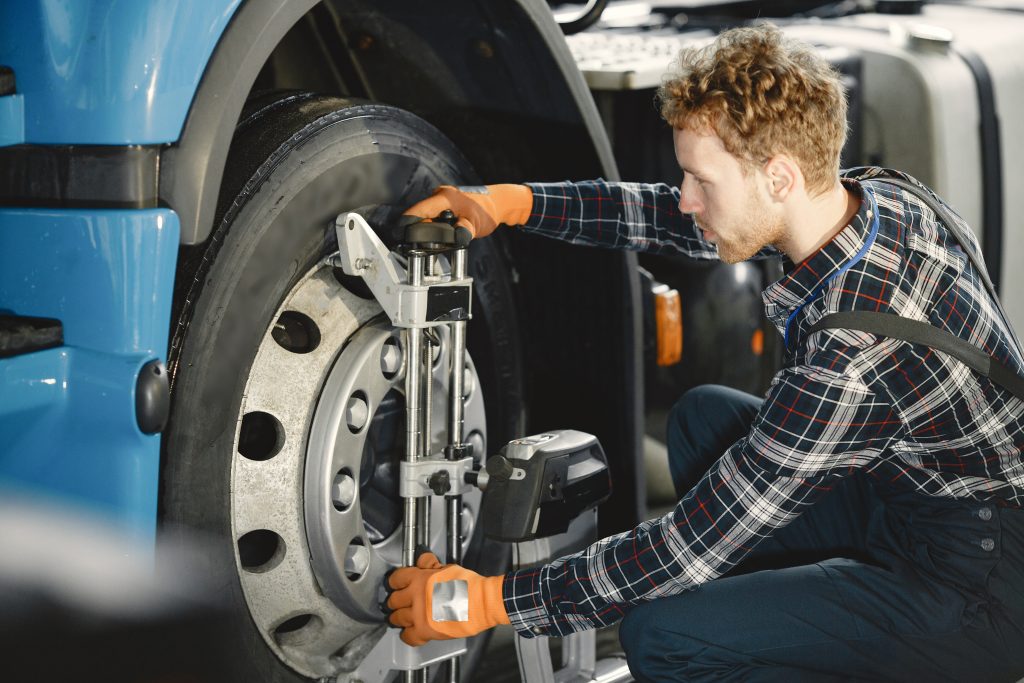 A mechanic performing an alignment check on a large truck to ensure proper tire positioning.